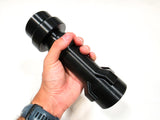 A hand holding a black plastic, futuristic flashlight-shaped object against a plain white background.
