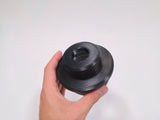 A hand holding a black 3D-printed cylindrical stud piece against a plain white background.