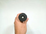 A hand holding a black cylindrical object with a textured circular top and a small white circular center, photographed against a plain white background.