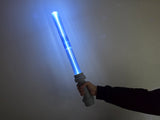 A hand holding a glowing blue plastic lightsaber-style toy against a plain wall.